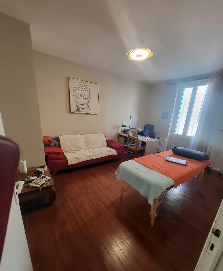 La salle de soin vue depuis la porte, avec le bureau de consultation et la table de soin près de la fenêtre